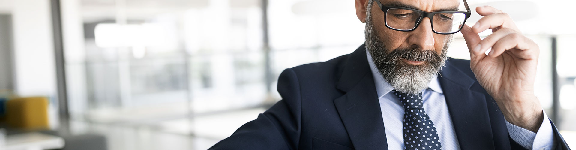 Cuentas Banca Privada - Asesor financiero con traje, corbata y gafas mirando una tablet sentado en una silla en la oficina Cuentas Banca Privada - Asesor financiero con traje, corbata y gafas mirando una tablet sentado en una silla en la oficina