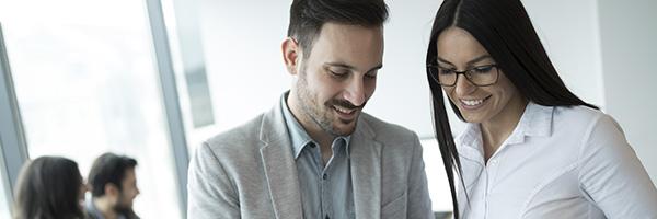 Asesoramiento Financiero - Compañeros de trabajo trabajando juntos en la oficina sonriendo y con una tablet en la mano